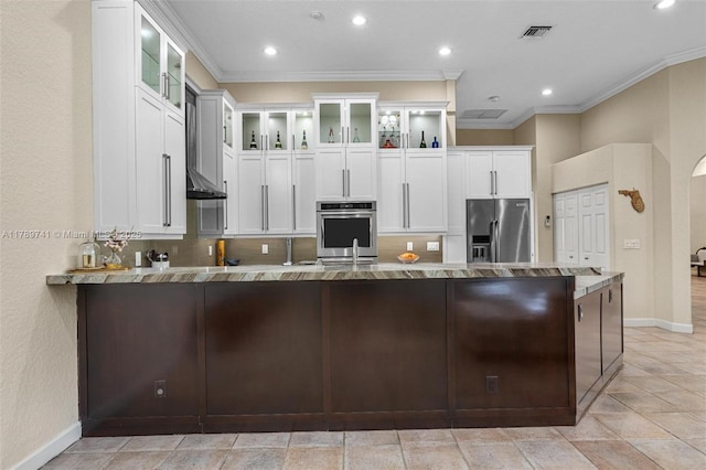 kitchen with crown molding, a peninsula, glass insert cabinets, light stone counters, and appliances with stainless steel finishes