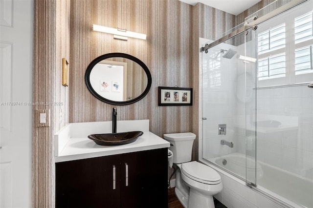 bathroom featuring toilet, wallpapered walls, combined bath / shower with glass door, and vanity