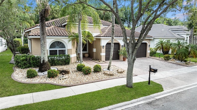 mediterranean / spanish house featuring an attached garage, stucco siding, driveway, and a tile roof