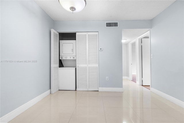 empty room with baseboards, stacked washing maching and dryer, light tile patterned floors, and visible vents