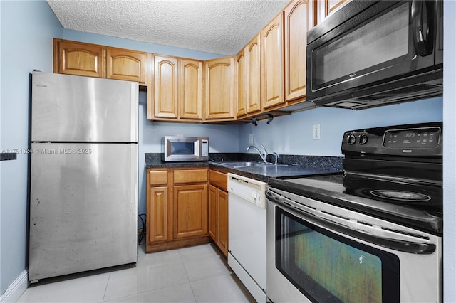 kitchen featuring a textured ceiling, a sink, light tile patterned floors, dark stone countertops, and stainless steel appliances