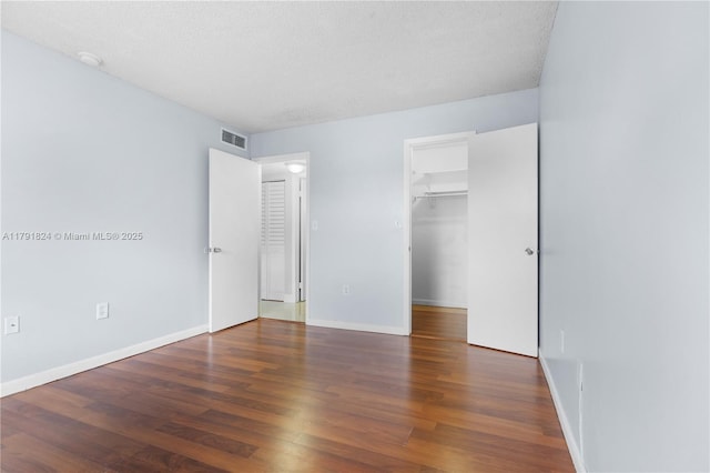 unfurnished bedroom with visible vents, wood finished floors, baseboards, a textured ceiling, and a spacious closet