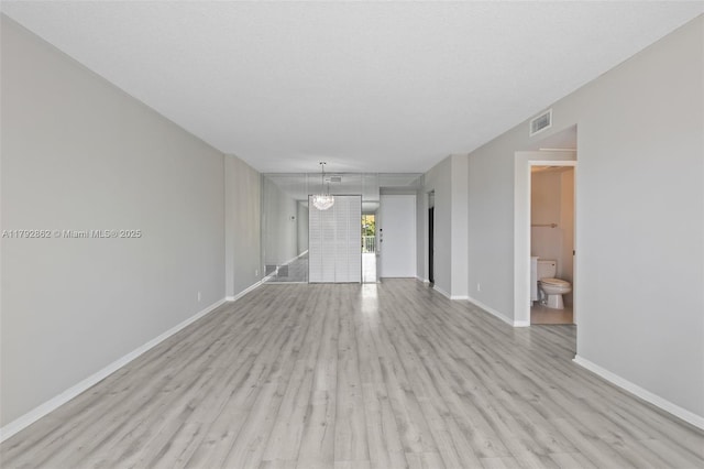 unfurnished living room with an inviting chandelier, baseboards, light wood-type flooring, and visible vents