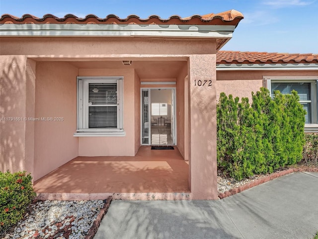 view of exterior entry with a patio, a tile roof, and stucco siding