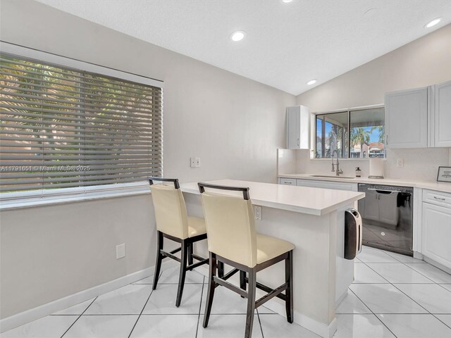 kitchen featuring lofted ceiling, a kitchen bar, light countertops, a sink, and dishwasher