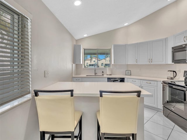 kitchen featuring a sink, light countertops, a kitchen breakfast bar, vaulted ceiling, and black appliances