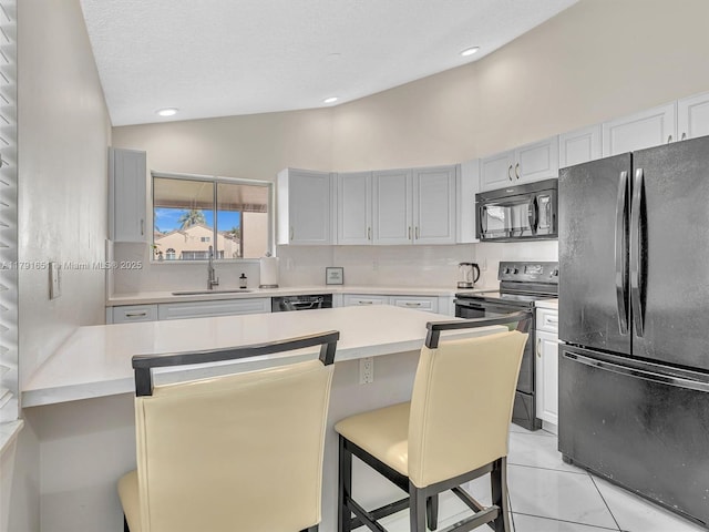 kitchen featuring a kitchen bar, vaulted ceiling, a sink, light countertops, and black appliances