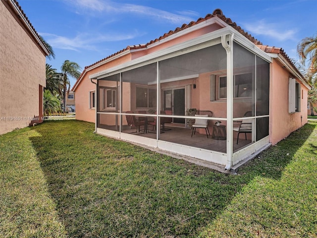 rear view of house with a sunroom, a lawn, and a tile roof