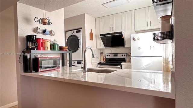 kitchen featuring stainless steel range with electric cooktop, stacked washer and dryer, a sink, freestanding refrigerator, and decorative backsplash