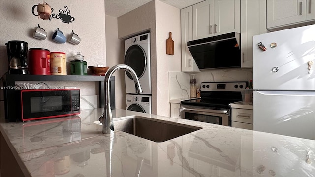 kitchen with stacked washer and dryer, black microwave, light stone counters, freestanding refrigerator, and electric stove