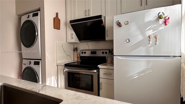 kitchen with tasteful backsplash, stainless steel range with electric cooktop, stacked washing maching and dryer, light countertops, and freestanding refrigerator