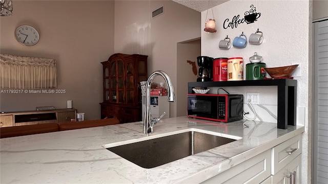 kitchen with visible vents, lofted ceiling, light stone countertops, white cabinets, and a sink