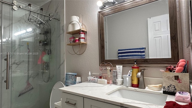 bathroom featuring a textured wall, a marble finish shower, and vanity