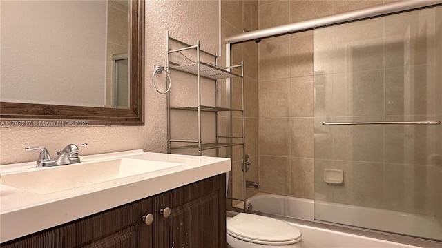 bathroom with vanity, a textured wall, toilet, and shower / bath combination with glass door