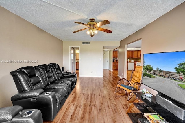 living area with visible vents, baseboards, light wood-type flooring, a textured ceiling, and a ceiling fan