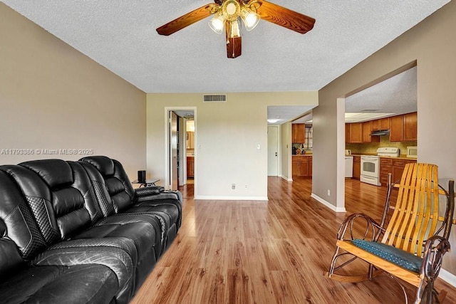 living room with visible vents, baseboards, light wood-type flooring, a textured ceiling, and a ceiling fan