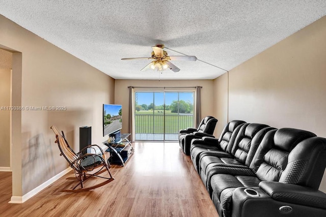 living room with a ceiling fan, a textured ceiling, baseboards, and light wood finished floors