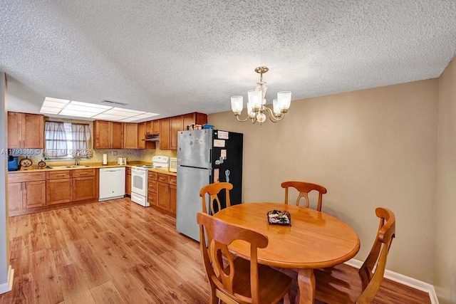 dining area with a textured ceiling, baseboards, light wood-style flooring, and a notable chandelier