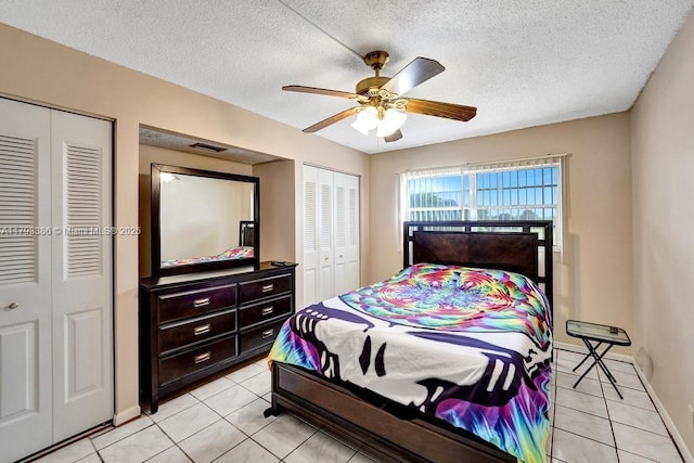 bedroom with a ceiling fan, a textured ceiling, multiple closets, and light tile patterned floors