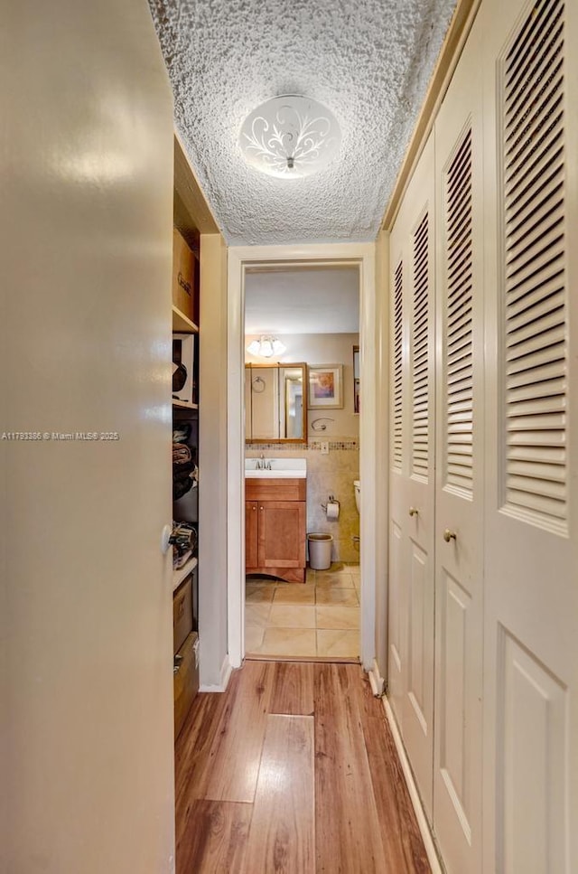 hallway with light wood-type flooring, a sink, and a textured ceiling