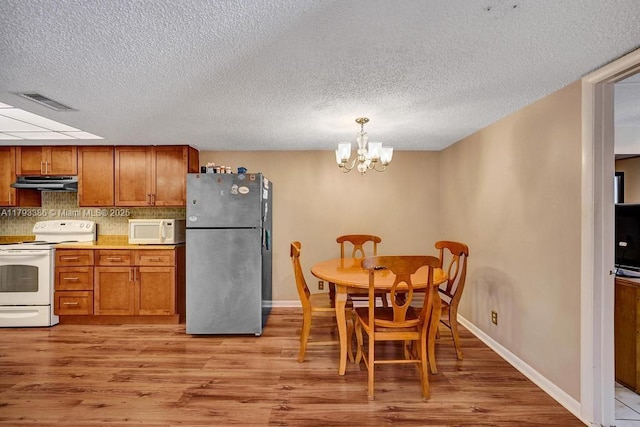 kitchen with exhaust hood, brown cabinetry, light wood-type flooring, a chandelier, and white appliances