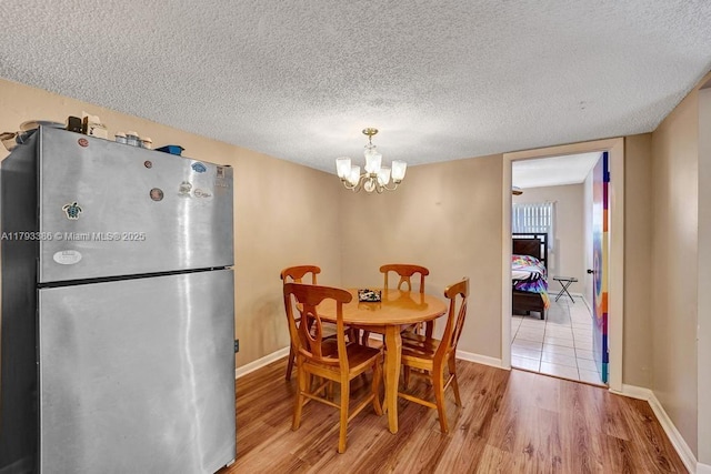 dining area featuring baseboards, a textured ceiling, wood finished floors, and a notable chandelier