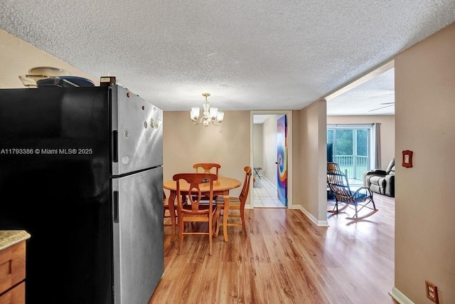 kitchen with freestanding refrigerator, a textured ceiling, an inviting chandelier, and light wood-style flooring