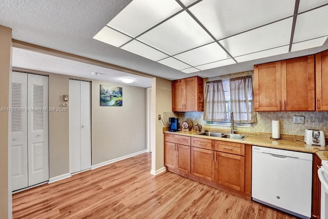 kitchen with white appliances, brown cabinetry, a sink, and light wood-style floors