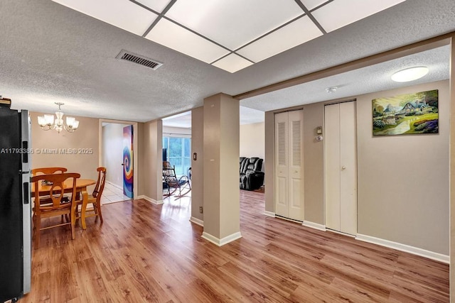 dining room with a textured ceiling, visible vents, light wood-type flooring, baseboards, and an inviting chandelier