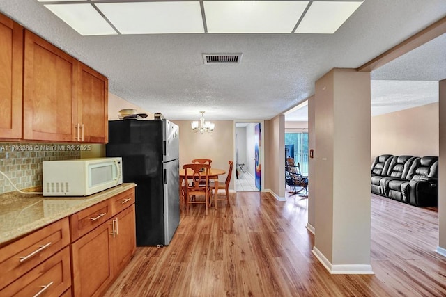 kitchen with visible vents, freestanding refrigerator, white microwave, light wood-type flooring, and brown cabinets