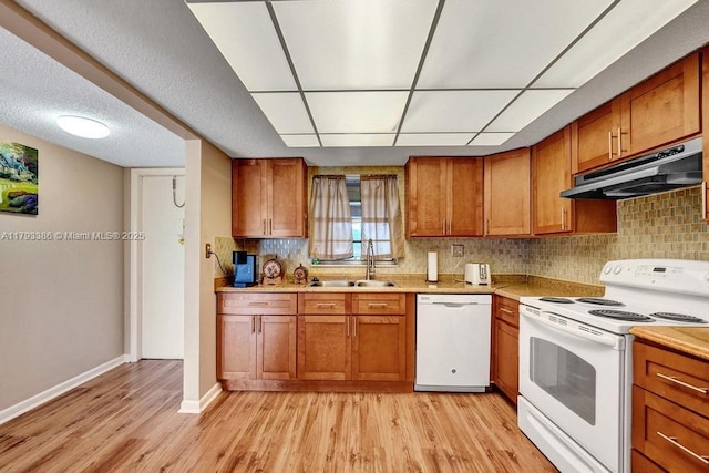 kitchen with brown cabinets, a sink, white appliances, light wood-style flooring, and under cabinet range hood