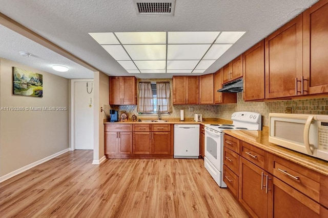 kitchen featuring brown cabinets, white appliances, baseboards, under cabinet range hood, and visible vents