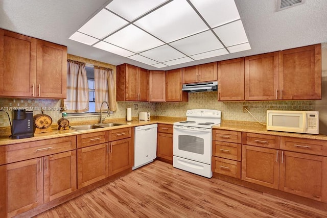 kitchen featuring visible vents, a sink, under cabinet range hood, white appliances, and light wood-style flooring