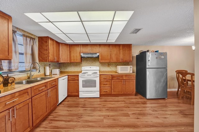 kitchen with brown cabinetry, white appliances, under cabinet range hood, a sink, and light wood-style flooring