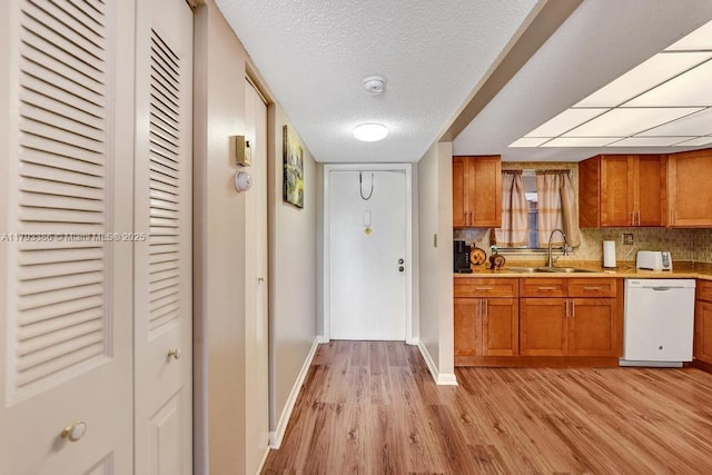 kitchen featuring brown cabinets, dishwasher, a sink, baseboards, and light wood-style flooring