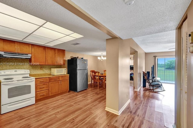 kitchen with a notable chandelier, white appliances, a textured ceiling, brown cabinetry, and under cabinet range hood