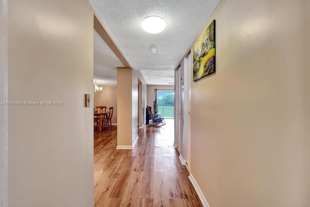 hall featuring baseboards, a textured ceiling, wood finished floors, and a notable chandelier