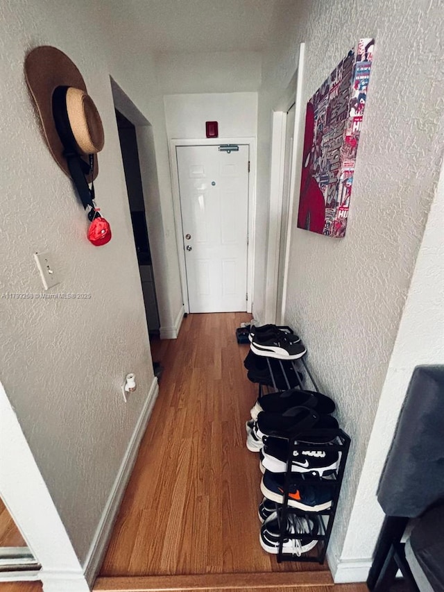 hallway featuring baseboards, a textured wall, and wood finished floors