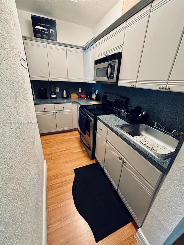 820 Euclid Ave Unit 206, Miami Beach, FL 33139 - kitchen featuring appliances with stainless steel finishes, a sink, white cabinets, backsplash, and a textured wall
