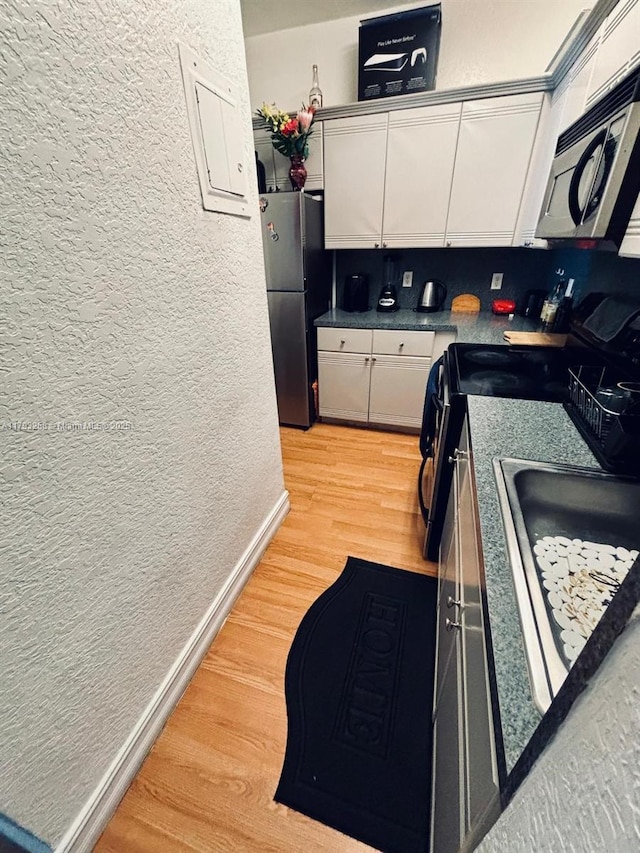 820 Euclid Ave Unit 206, Miami Beach, FL 33139 - kitchen with a textured wall, freestanding refrigerator, light wood finished floors, white cabinets, and baseboards