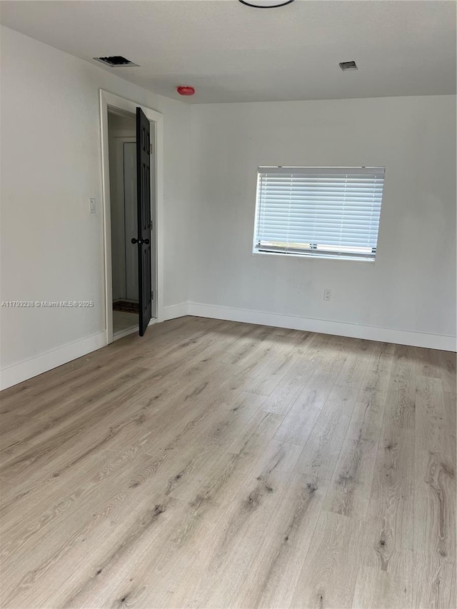 spare room with baseboards, visible vents, and wood finished floors