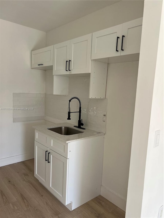 kitchen with backsplash, white cabinets, a sink, and light wood-type flooring