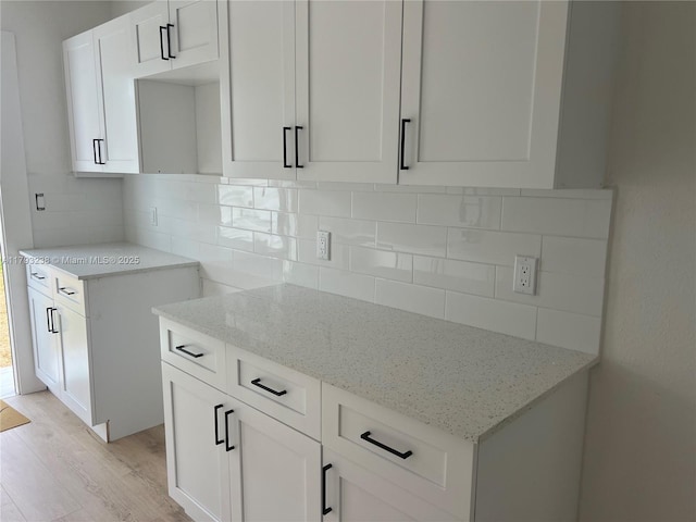 kitchen with light wood-type flooring, white cabinetry, light stone countertops, and tasteful backsplash