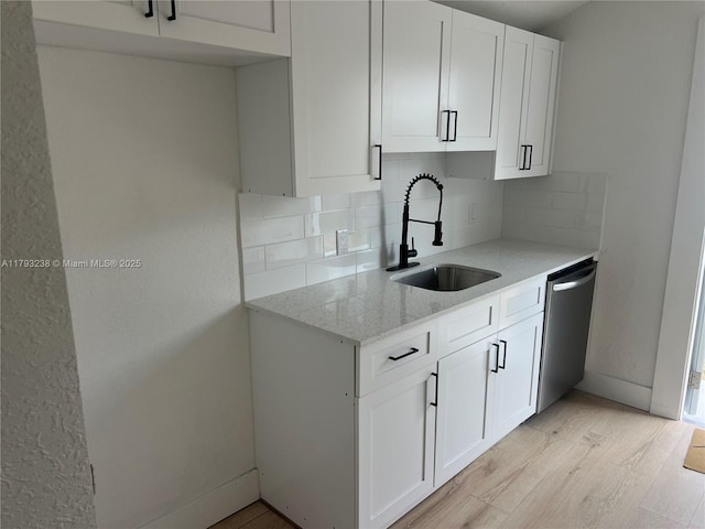 kitchen featuring backsplash, light stone countertops, dishwasher, a sink, and white cabinetry