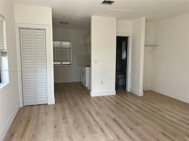 unfurnished bedroom with baseboards, a closet, attic access, and light wood-style flooring