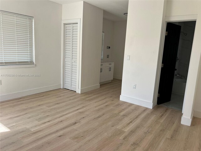 unfurnished bedroom featuring baseboards, a closet, light wood finished floors, and connected bathroom