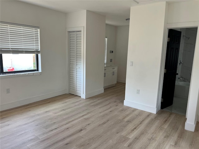 unfurnished bedroom with a closet, baseboards, ensuite bathroom, and light wood-type flooring