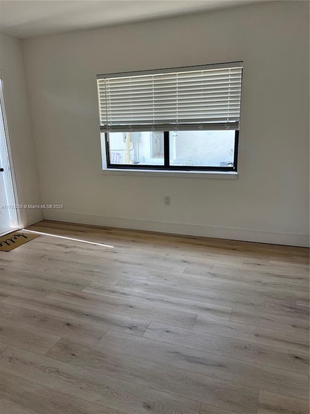 spare room featuring baseboards, wood finished floors, and a healthy amount of sunlight