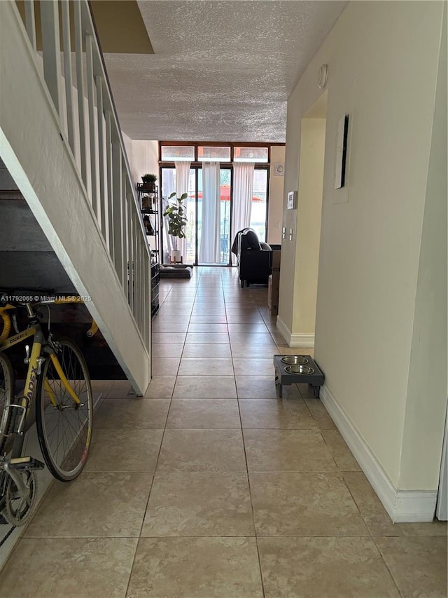 hall featuring light tile patterned floors, a textured ceiling, stairway, baseboards, and floor to ceiling windows