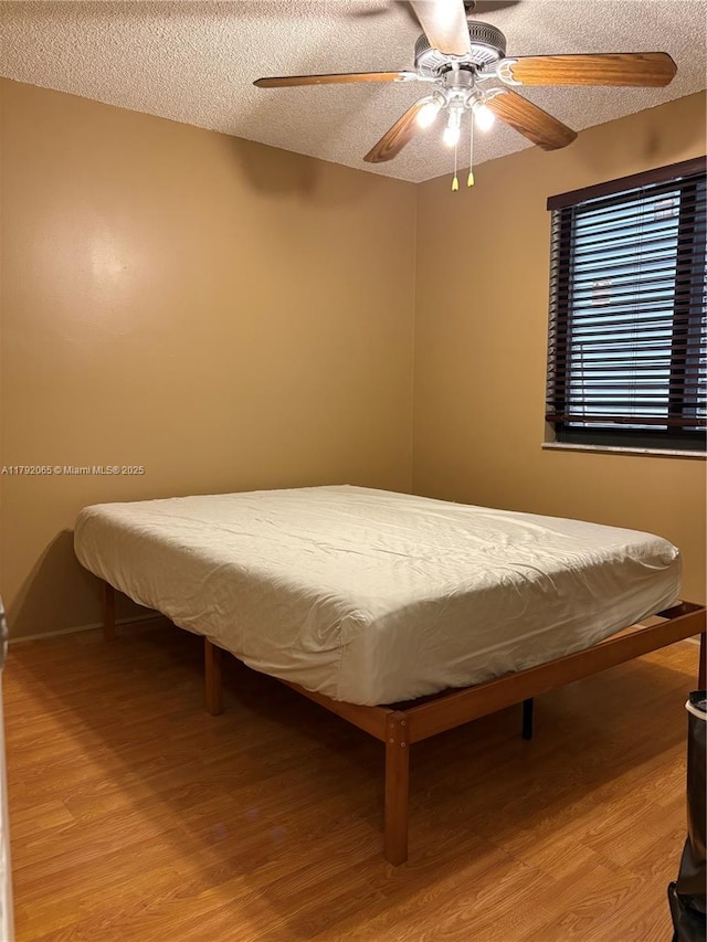 bedroom with a textured ceiling, a ceiling fan, and wood finished floors